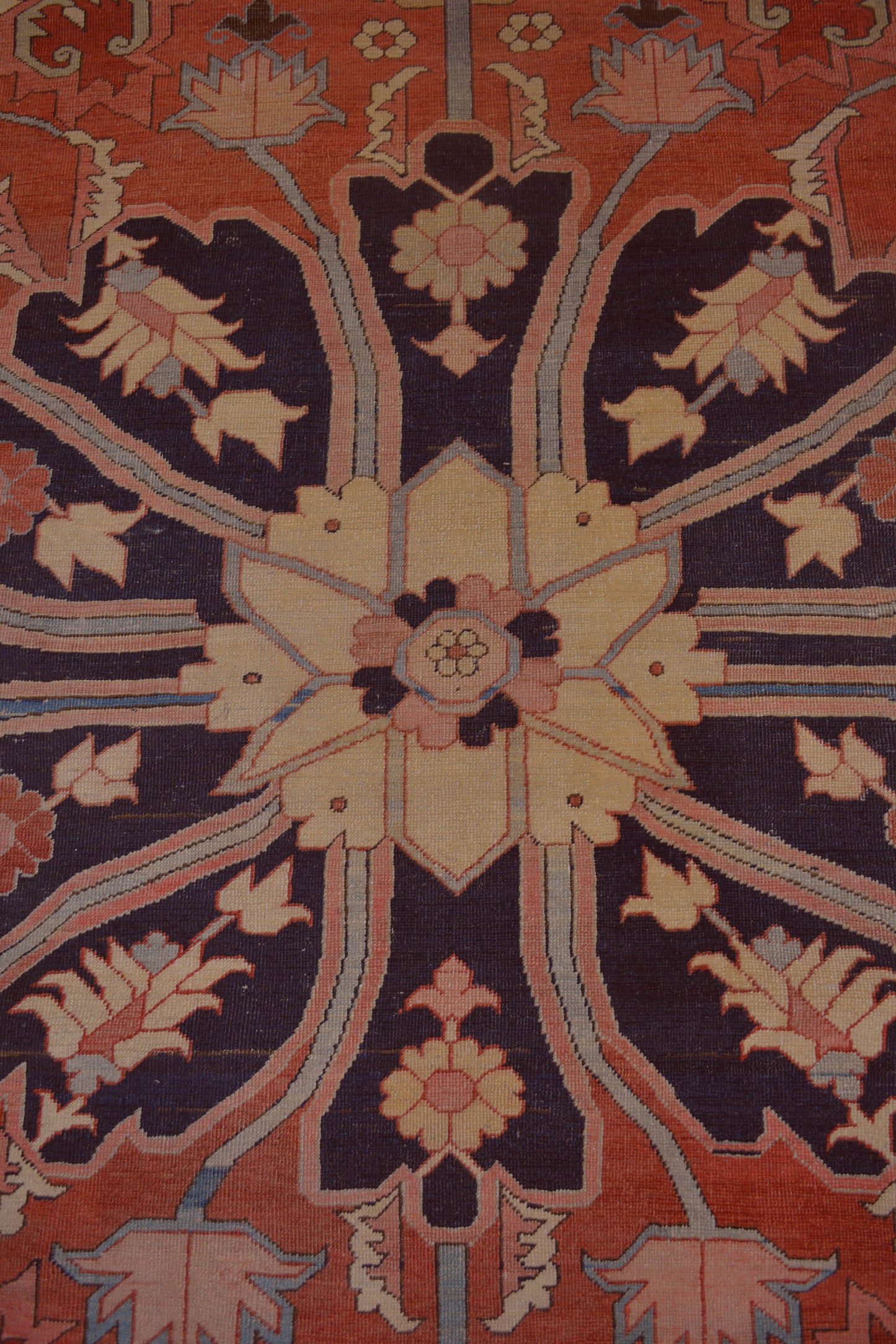 The central focal area has a large black flower holding a secondary beige flower in the middle, and the same design is placed in each corner of the central area of the rug.