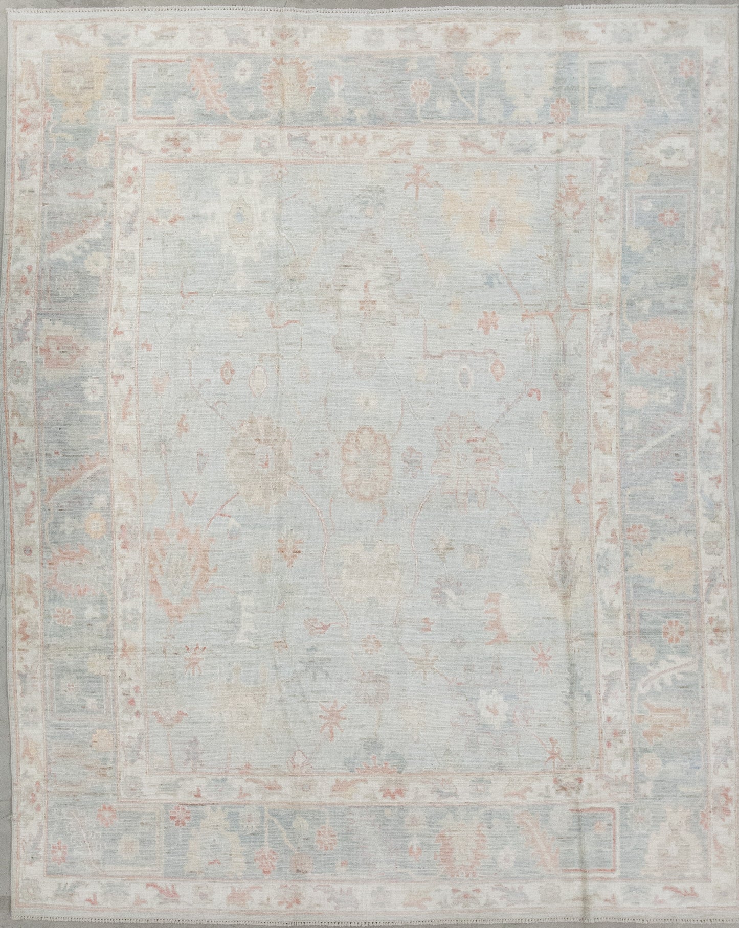 A sophisticated rug was woven in shades of beige as the dominant color, with orange, red, blue and white as contrasts. The design features abstract red and white poppies, sunflowers, and branches all around it.