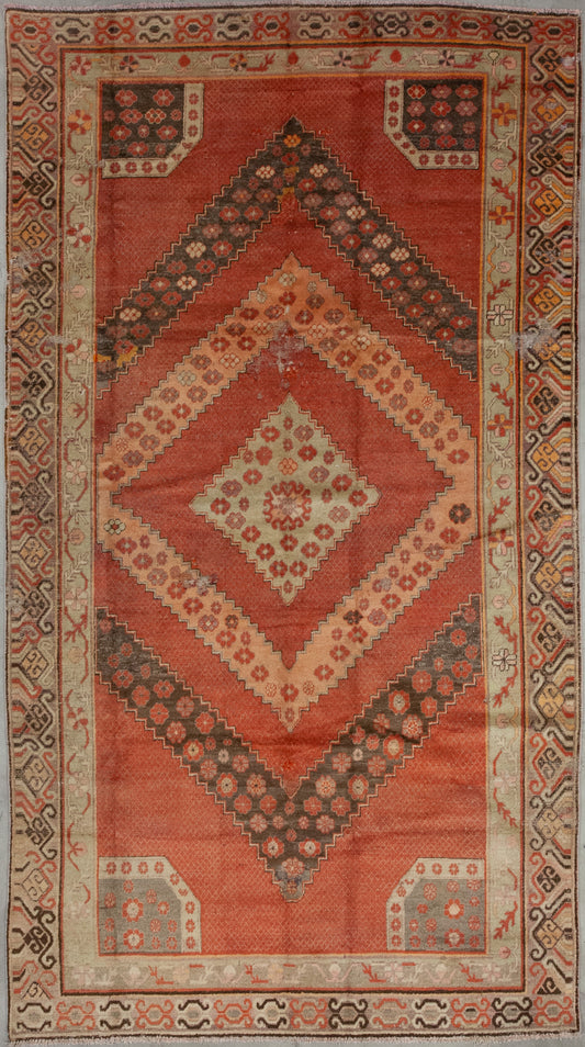 This impressive carpet was woven with a warmth color scheme which has orange for the central background, beige for the contour, and gray for the details. The design features a large rhomb with more nested diamond shapes which are patterned with small flower heads.